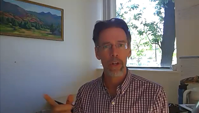 Photo of a man speaking, window with tree in the background.