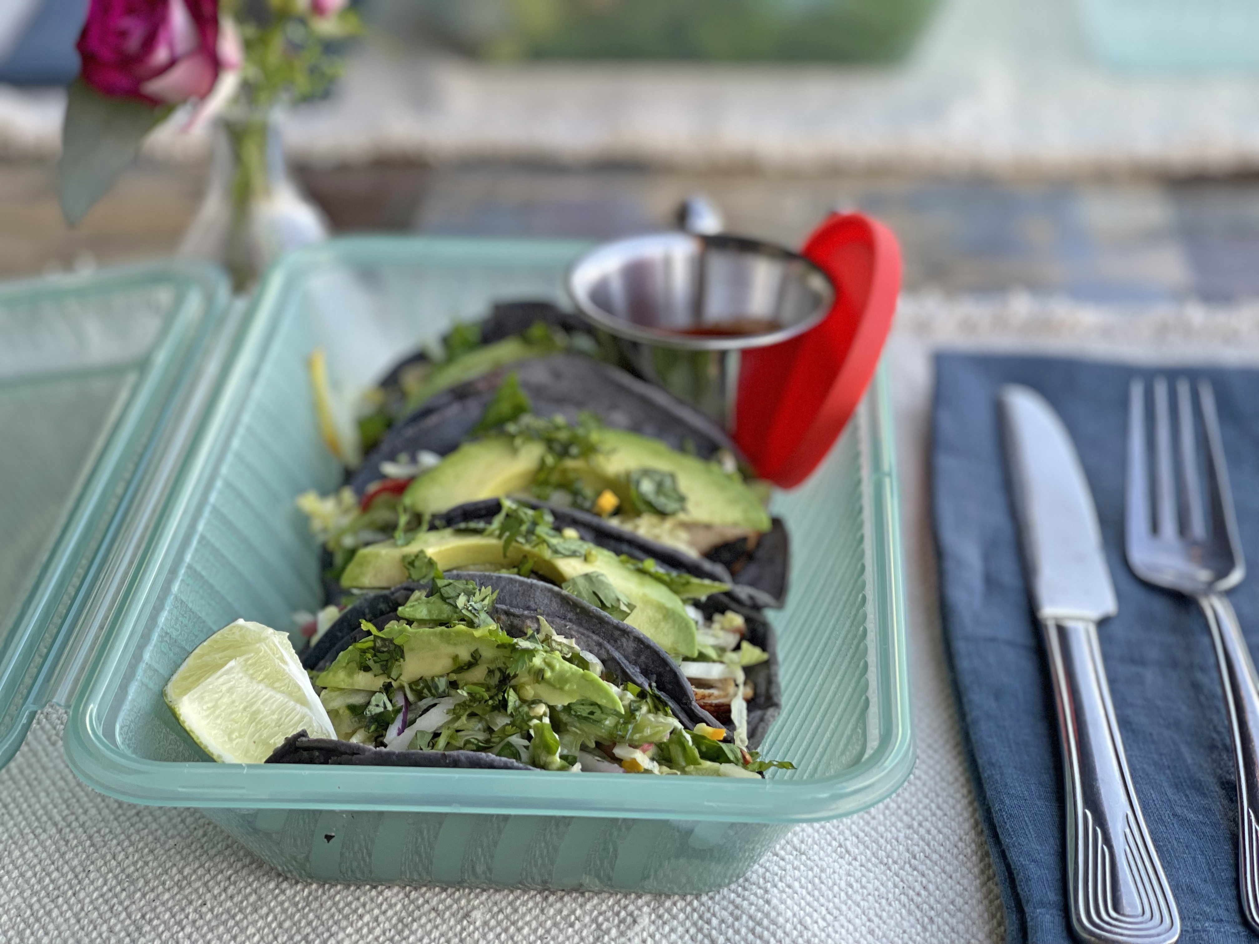 Four tacos in a reusable container on a set table