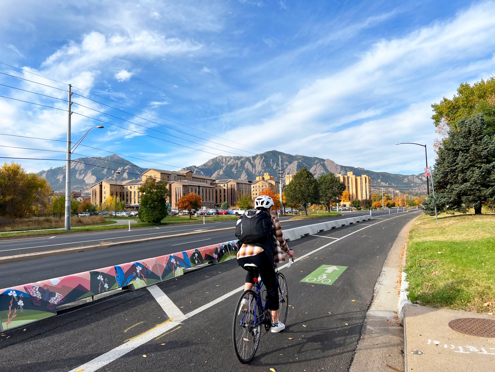 A person biking on the Baseline Road bike lane next to tall curbs with mural art