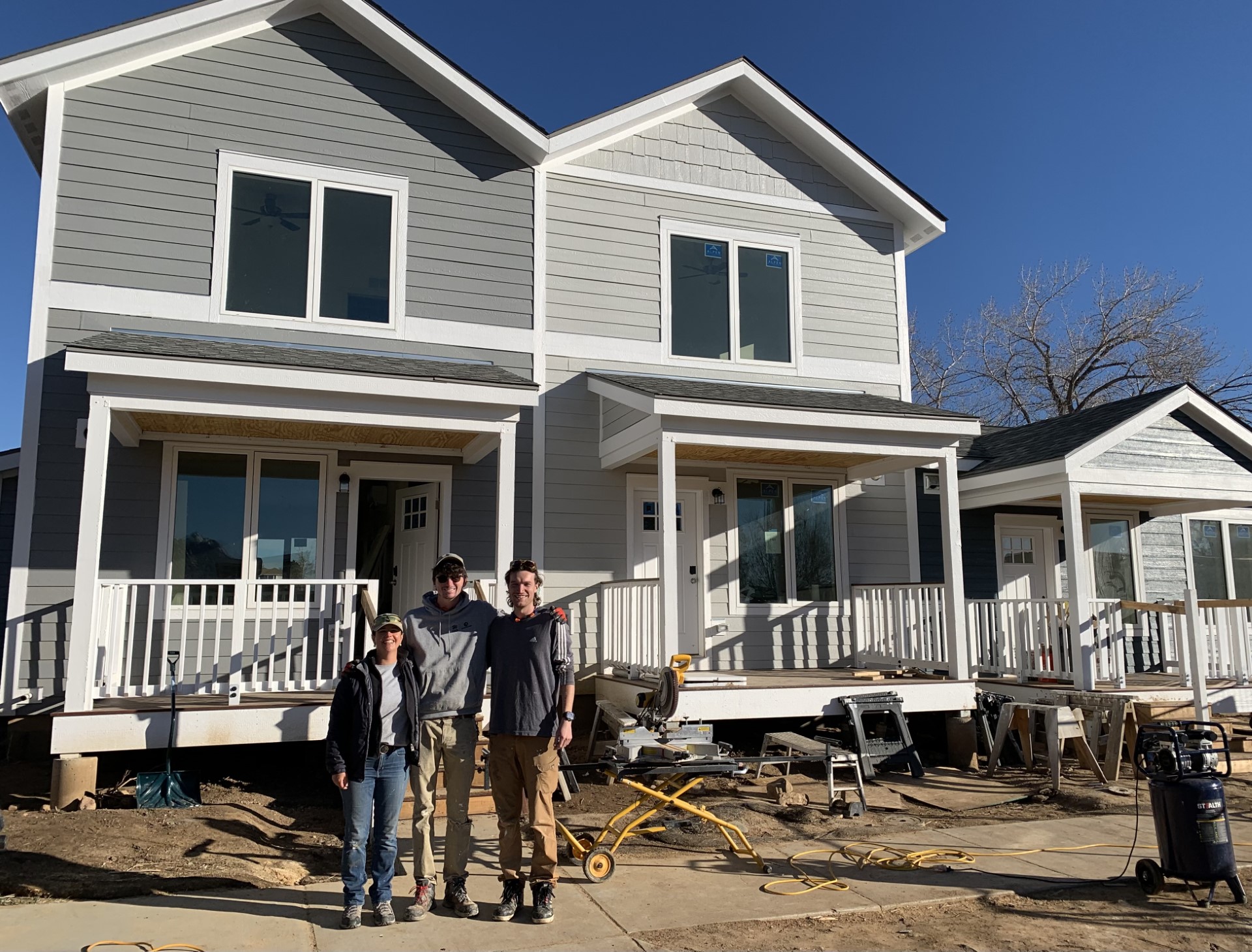 Three Habitat for Humanity volunteers standing in front of nearly completed new homes at Ponderosa.