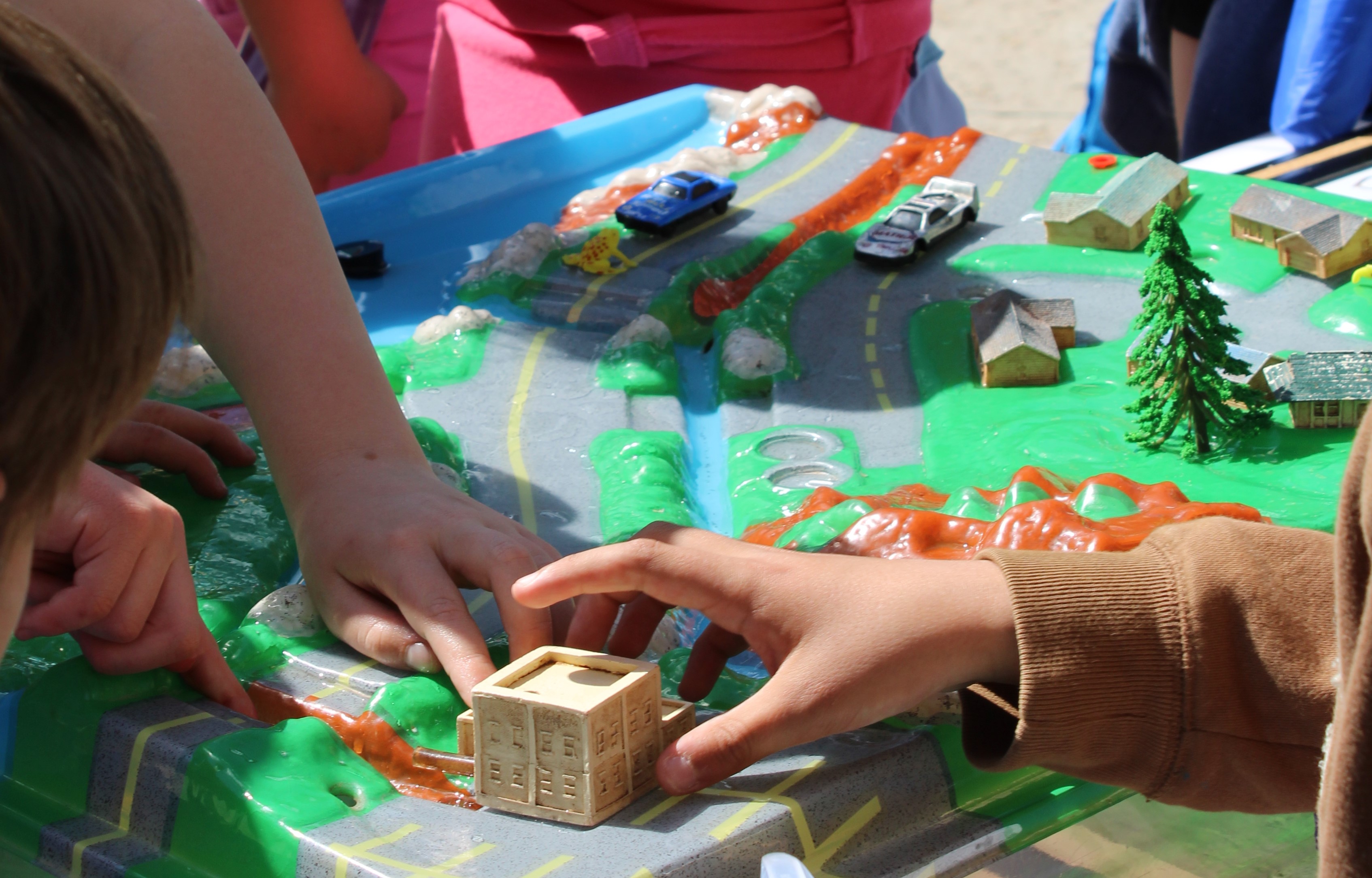 Children interacting with blocks for cars and houses and trees on a sculpted diorama of a suburban landscape