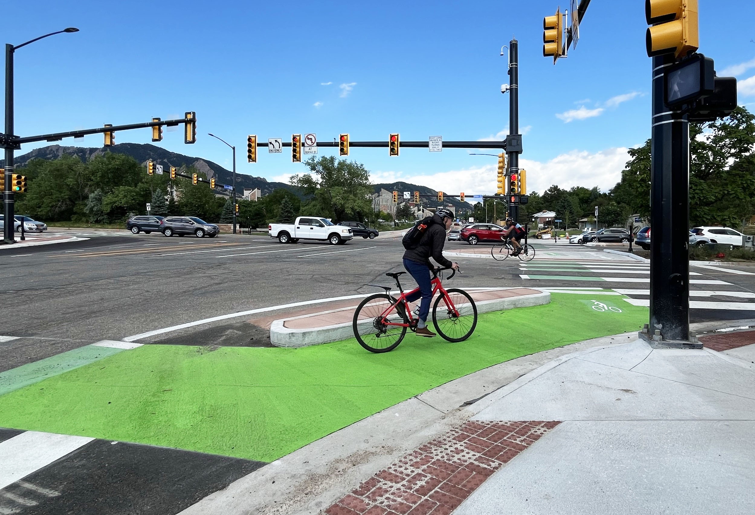 Person biking next to corner island on protected bike lane at intersection