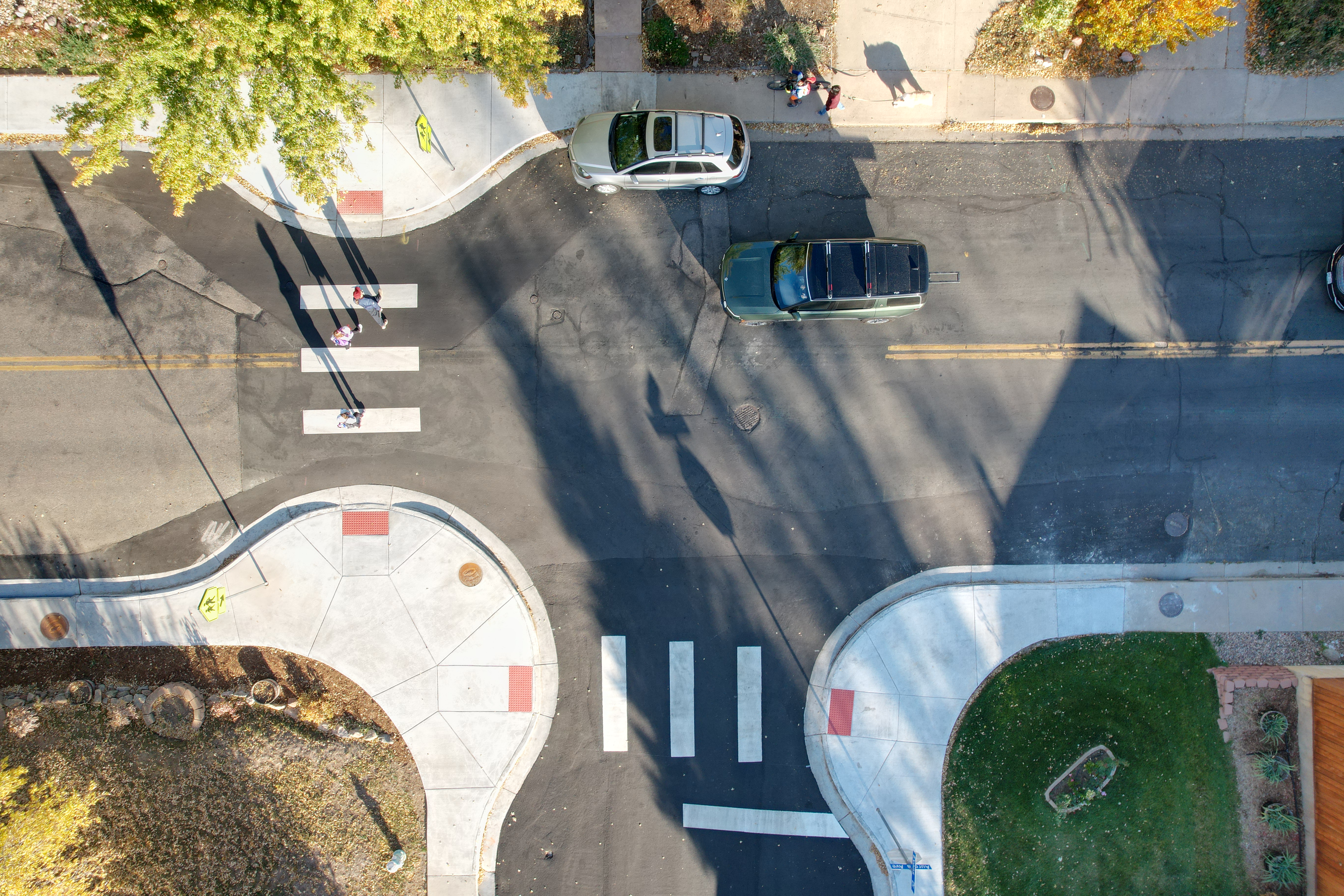 An overhead image of the Aurora Avenue and Evans Drive crosswalk with people walking across the crosswalk. Concrete curb extensions help shorten their crossing distance as a person driving yields. 