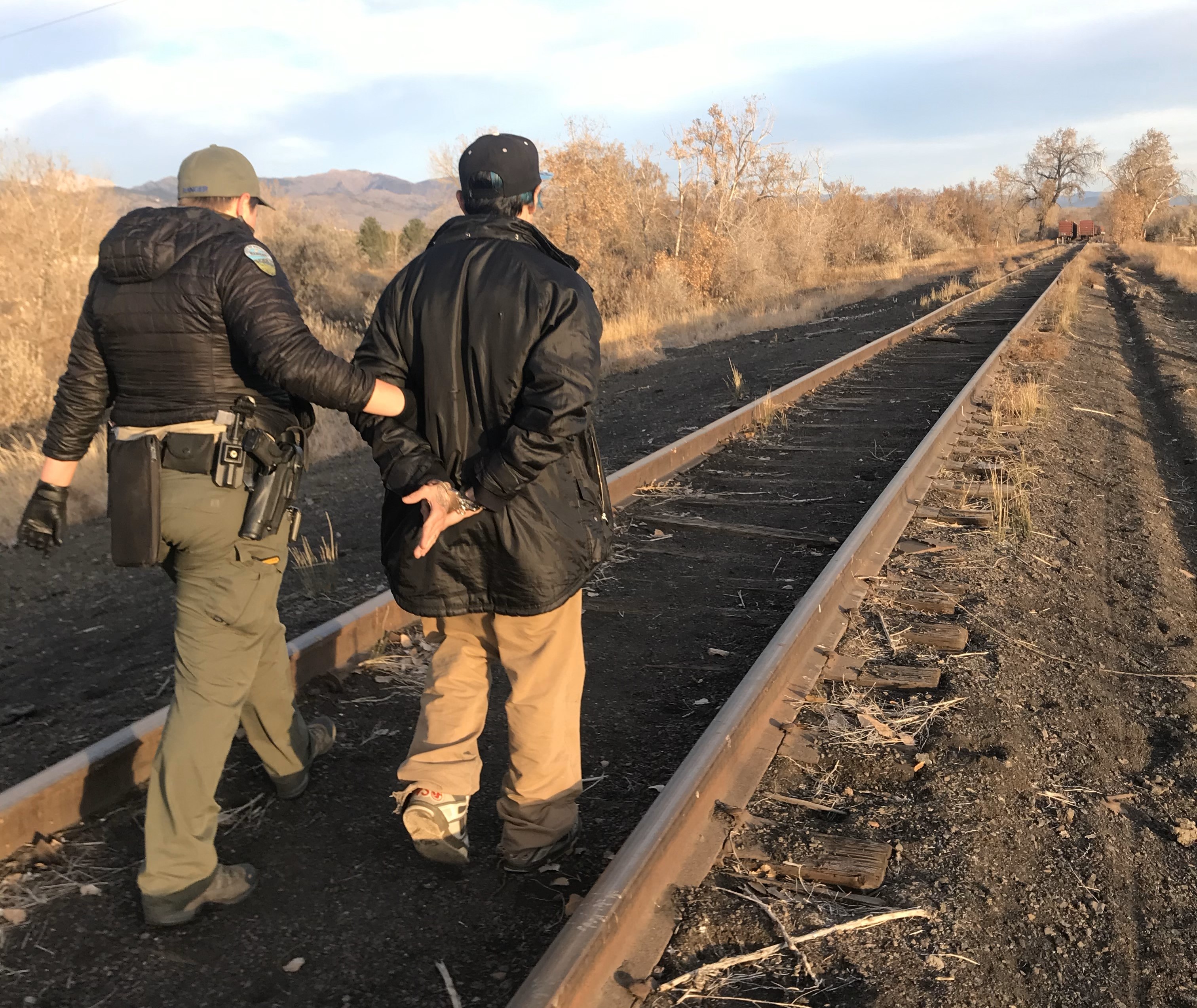 Ranger with suspect in custody walking down train tracks.