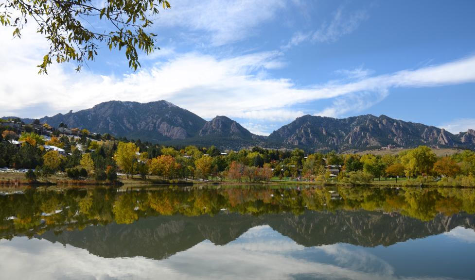 Distant view of the Flatirons with trees and water in closer view