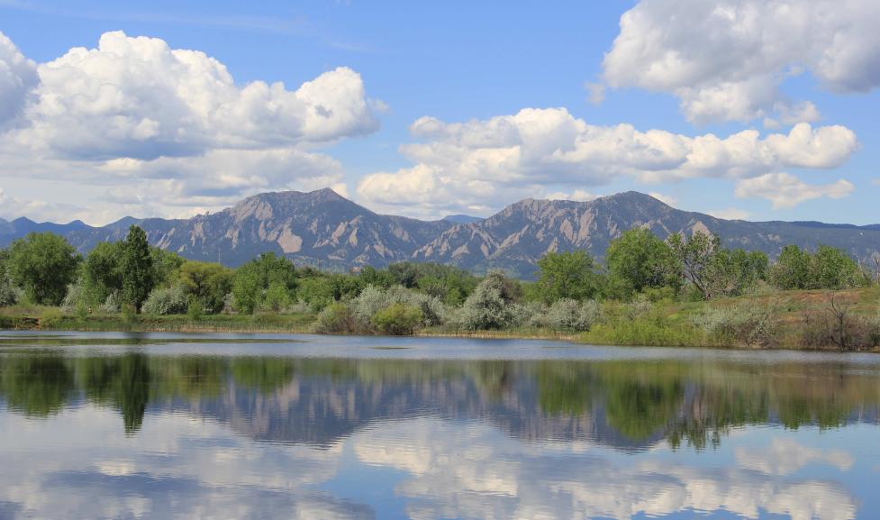 Sawhill Ponds in spring reflecting bright green trees, flatirons and white clouds in the water