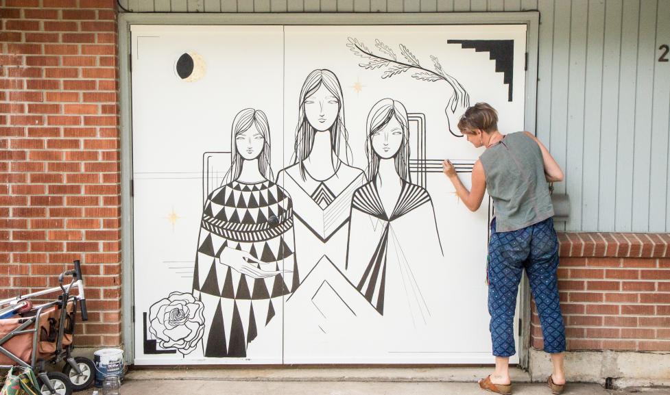 Artist installing mural artwork on a garage door