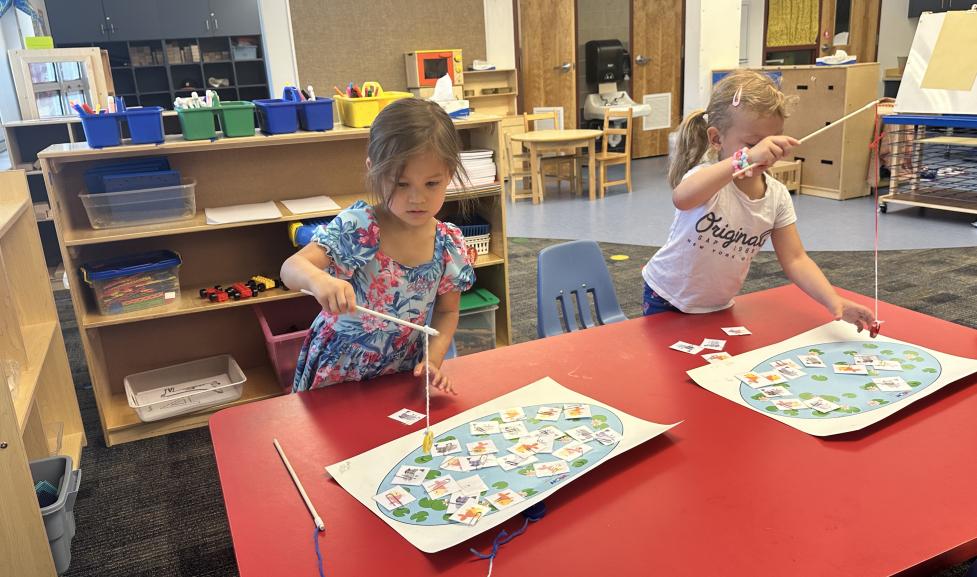 Two young students playing a fishing game on a school table.