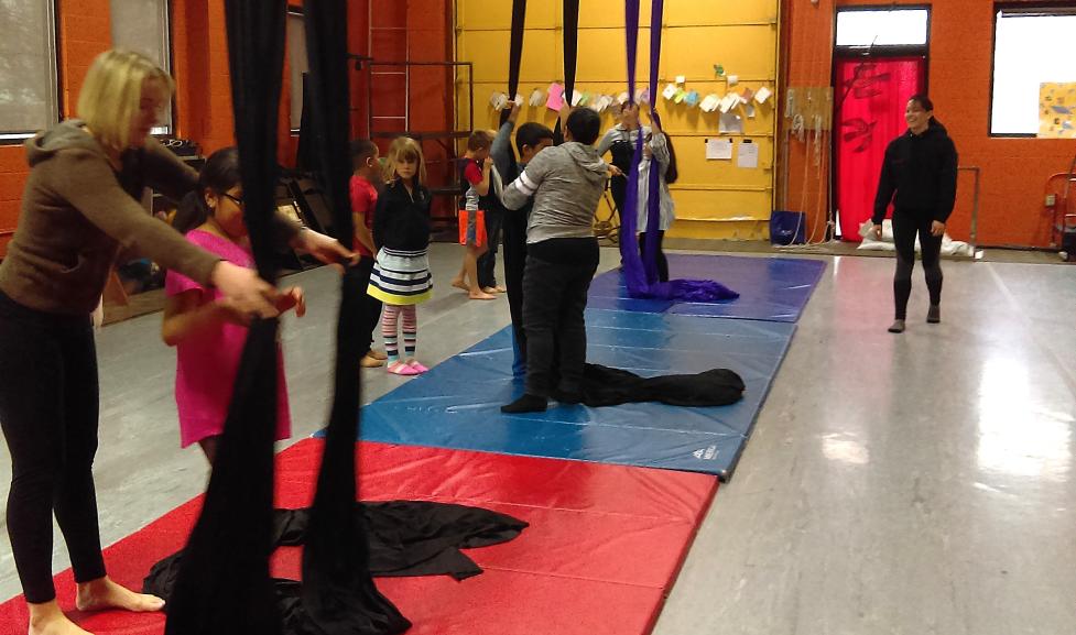 Adult instructors help kids with aerial silks in a gymnasium 