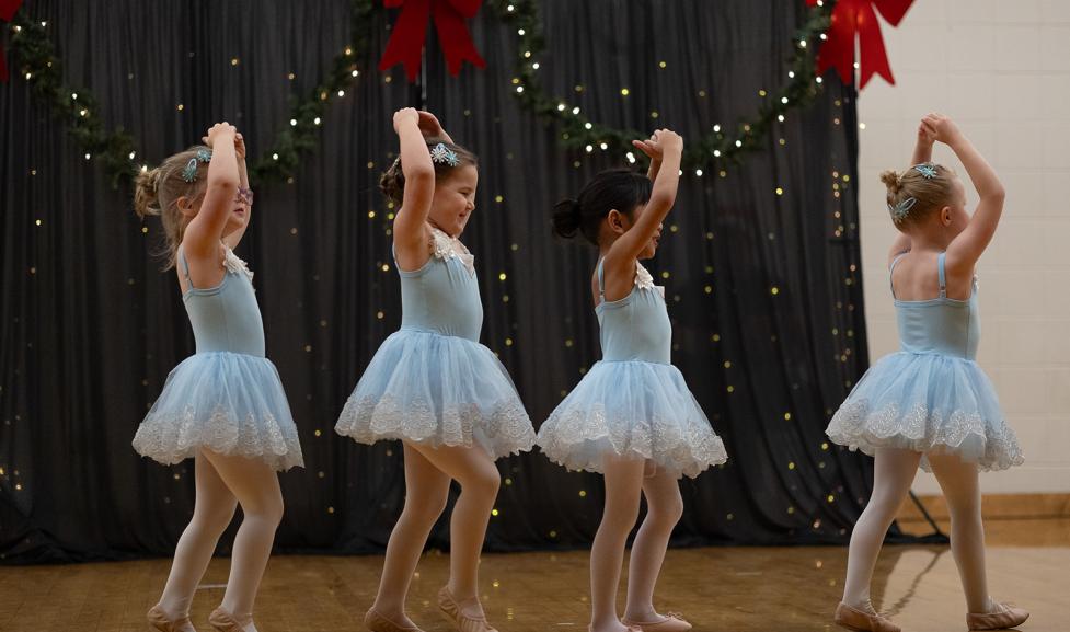 four dancers in blue dresses tiptoe in a line