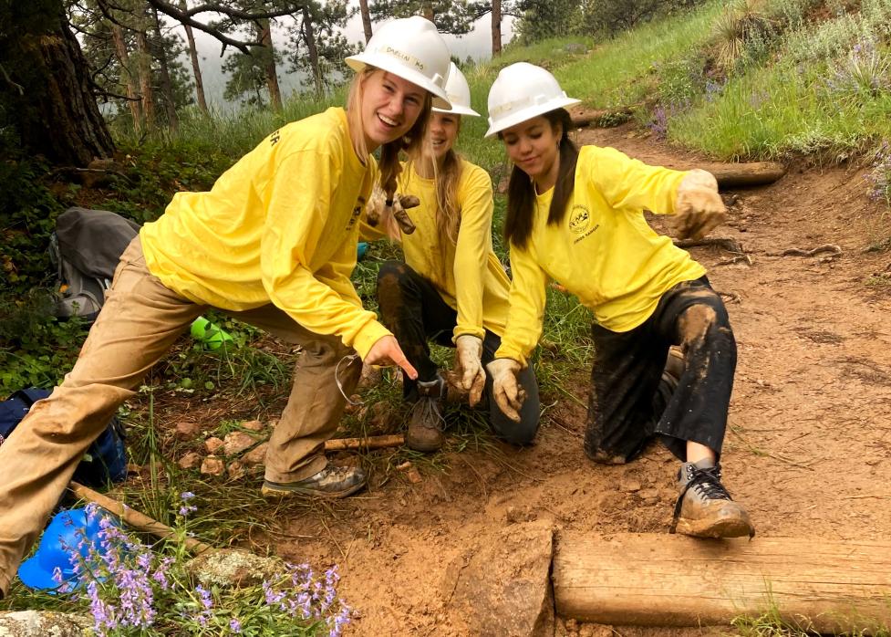 Three Junior Rangers proudly point towards a buried rock in the trail