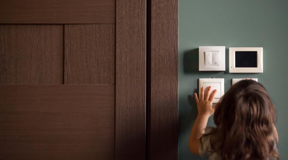 A brown-haired young girl fiddles with the thermostat in her home