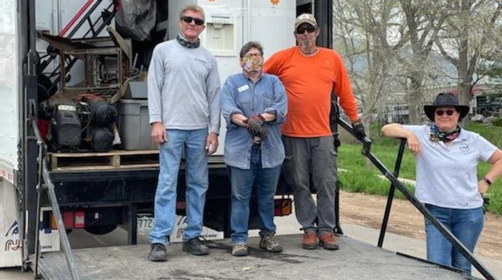 Photo of a large truck with appliances inside, four people are standing in front.