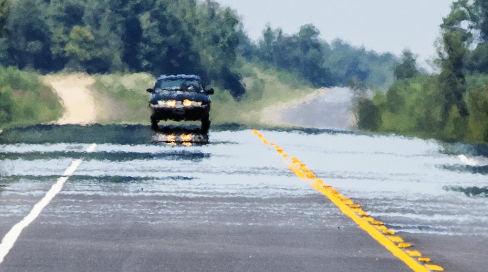 Heat rising from the road distorts the image of a car traveling on a road.