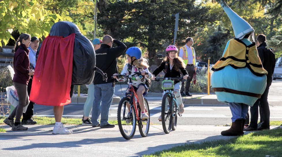 Kids biking and smiling at BVSD mascots. 