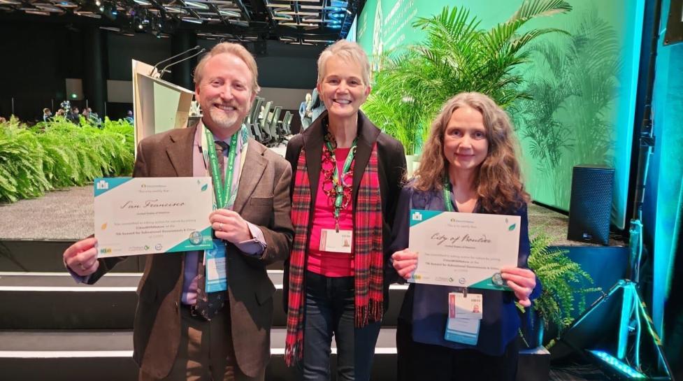 Rella Abernathy holds Boulder's Cities with Nature certificate alongside two other delegrates