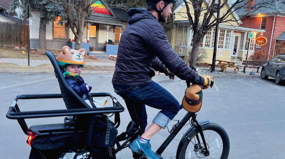 A person biking on an e-cargo bike with a child in the backseat