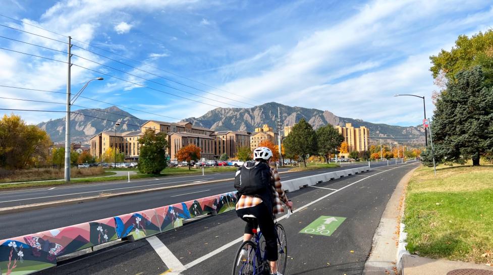 A person biking on the Baseline Road bike lane next to tall curbs with mural art