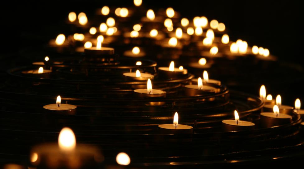 Dozens of lit tea light candles floating on water against a black background