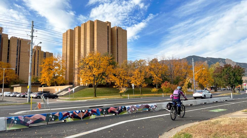 Person biking along tall, concrete curbs with mural art at Baseline Road near 32nd Street as part of earlier Phase 1 improvements