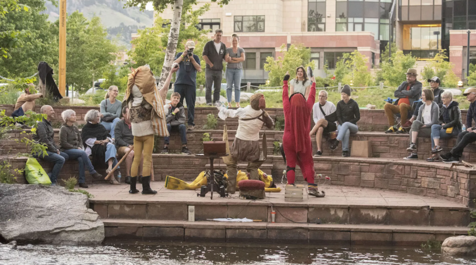 Performers dressed in costume acting for an audience next to the Boulder Creek