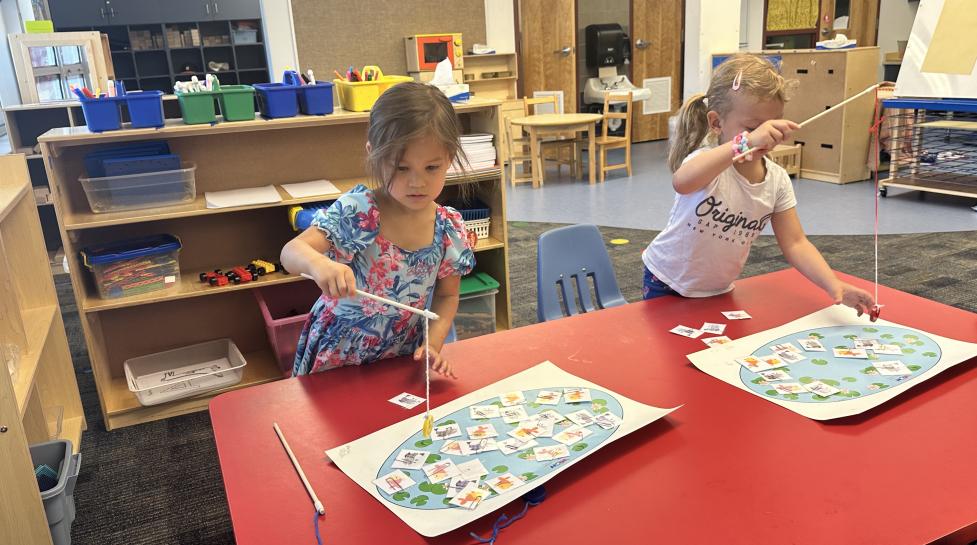 Two young students playing a fishing game on a school table.