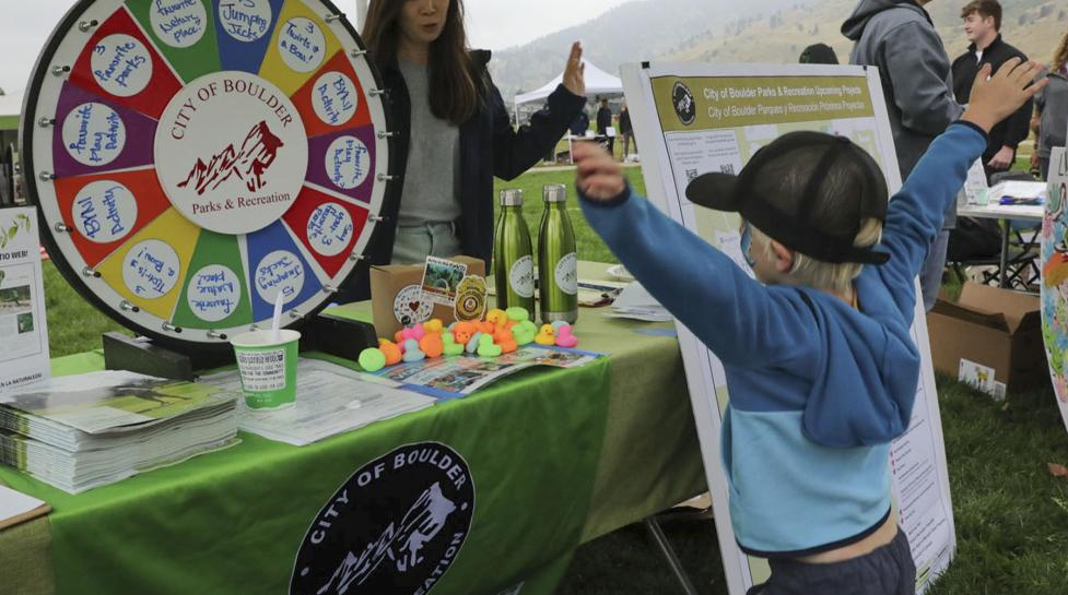 Parks and Recreation table with colorful spinning wheel and a young boy in front of the table with his hands in the air excited about winning something. 