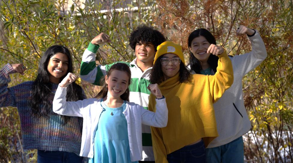 Children of different races standing together and smiling while flexing their arms to show their strength.