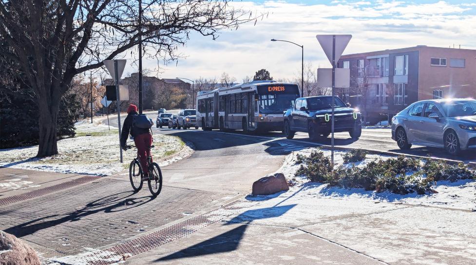 Person biking across crosswalk near Broadway while express bus and cars line up at traffic signal