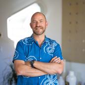 A man in a blue shirt with crossed arms is smiling at the camera.