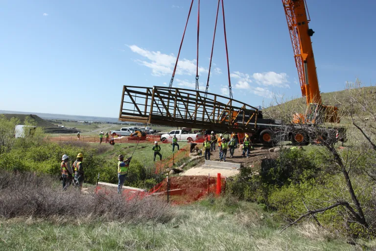 A large crane lowers a metal bridge over Schneider Draw to connect the North Sky Trail