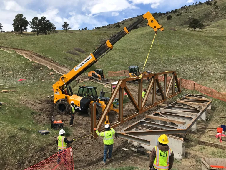 Construction equipment lifts a piece of the South Bridge over the North Sky Trail