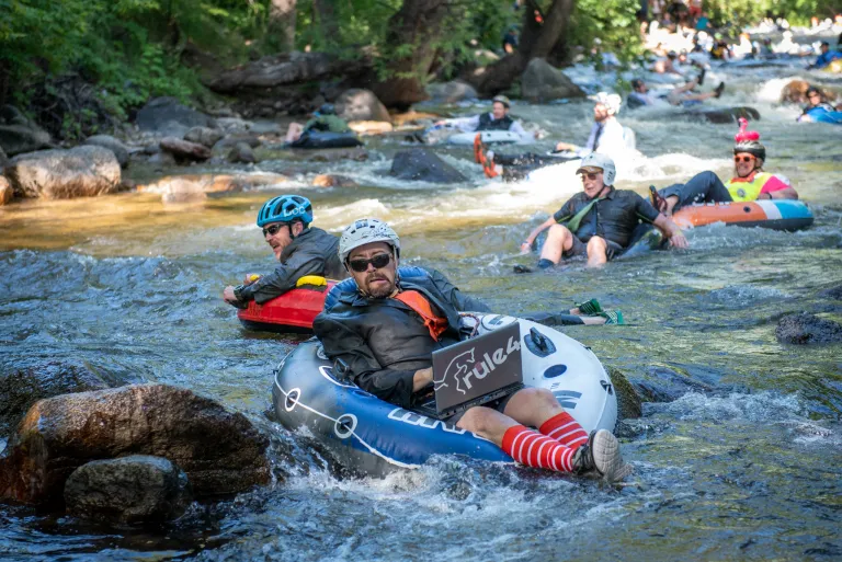 Person wearing a suit and holding a fake laptop tubing down the Boulder Creek