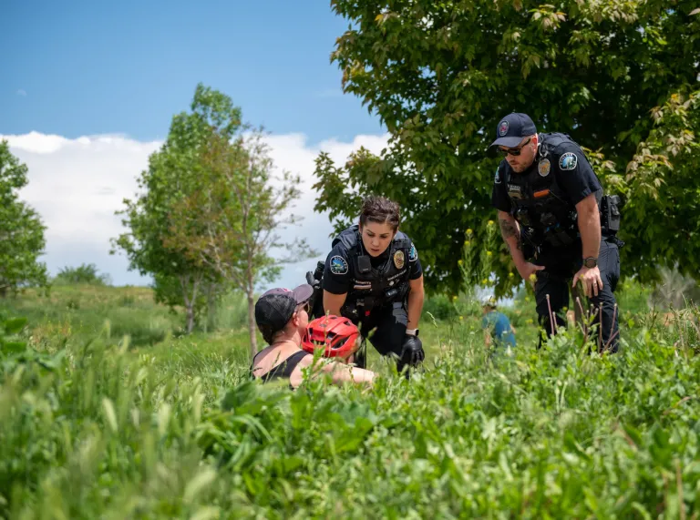 A male and female police officers bending over to talk with a woman and a child wearing a bicycle helmet on one of Boulder’s creek paths.