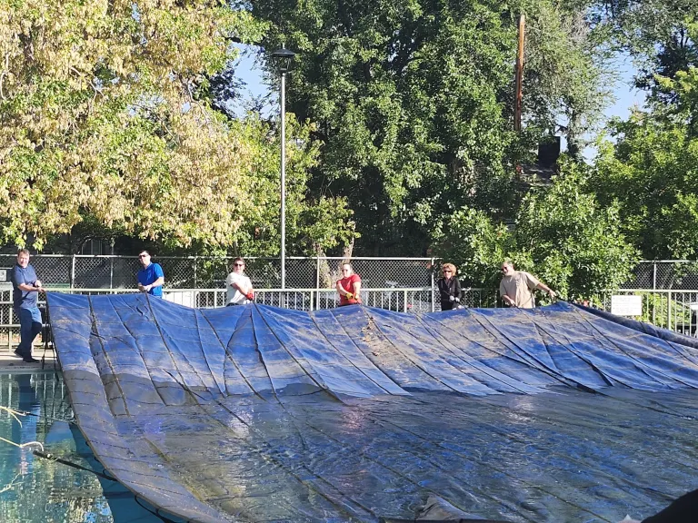 Six city staff members pulling a cover over the Spruce Street swimming pool.