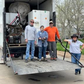 Photo of a large truck with appliances inside, four people are standing in front.