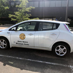 A Open Space and Mountain Parks electric vehicle sits in a parking lot