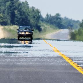 Heat rising from the road distorts the image of a car traveling on a road.