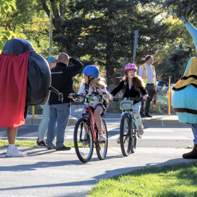 Kids biking and smiling at BVSD mascots. 