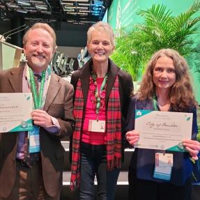 Rella Abernathy holds Boulder's Cities with Nature certificate alongside two other delegrates