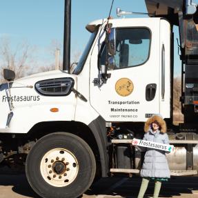 A child holding a magnet that says Frostasaurus smiles while standing next to a snowplow