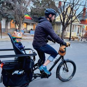 A person biking on an e-cargo bike with a child in the backseat