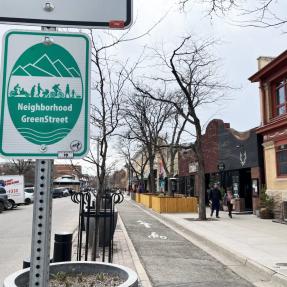 A neighborhood greenstreet sign next to a protected bike lane and sidewalk