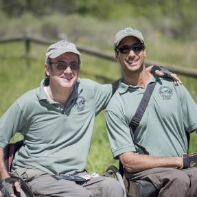 Two wheelchair users who are City of Boulder employees smiling at the camera while enjoying a roll on an accessible trail. 