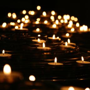 Dozens of lit tea light candles floating on water against a black background