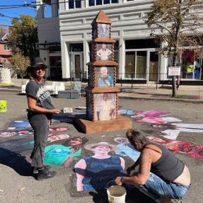 The artist standing in front of the wheat paste art project outside on a sunny day