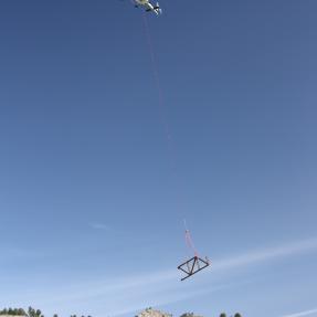 A helicopter flies overhead carrying a piece of metal bridge for North Sky Trail