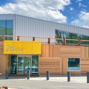 An architecturally unique building with horizontal and vertical wooden face panels and a bright yellow sign.