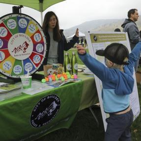 Parks and Recreation table with colorful spinning wheel and a young boy in front of the table with his hands in the air excited about winning something. 