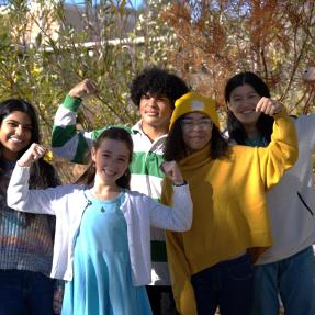 Children of different races standing together and smiling while flexing their arms to show their strength.